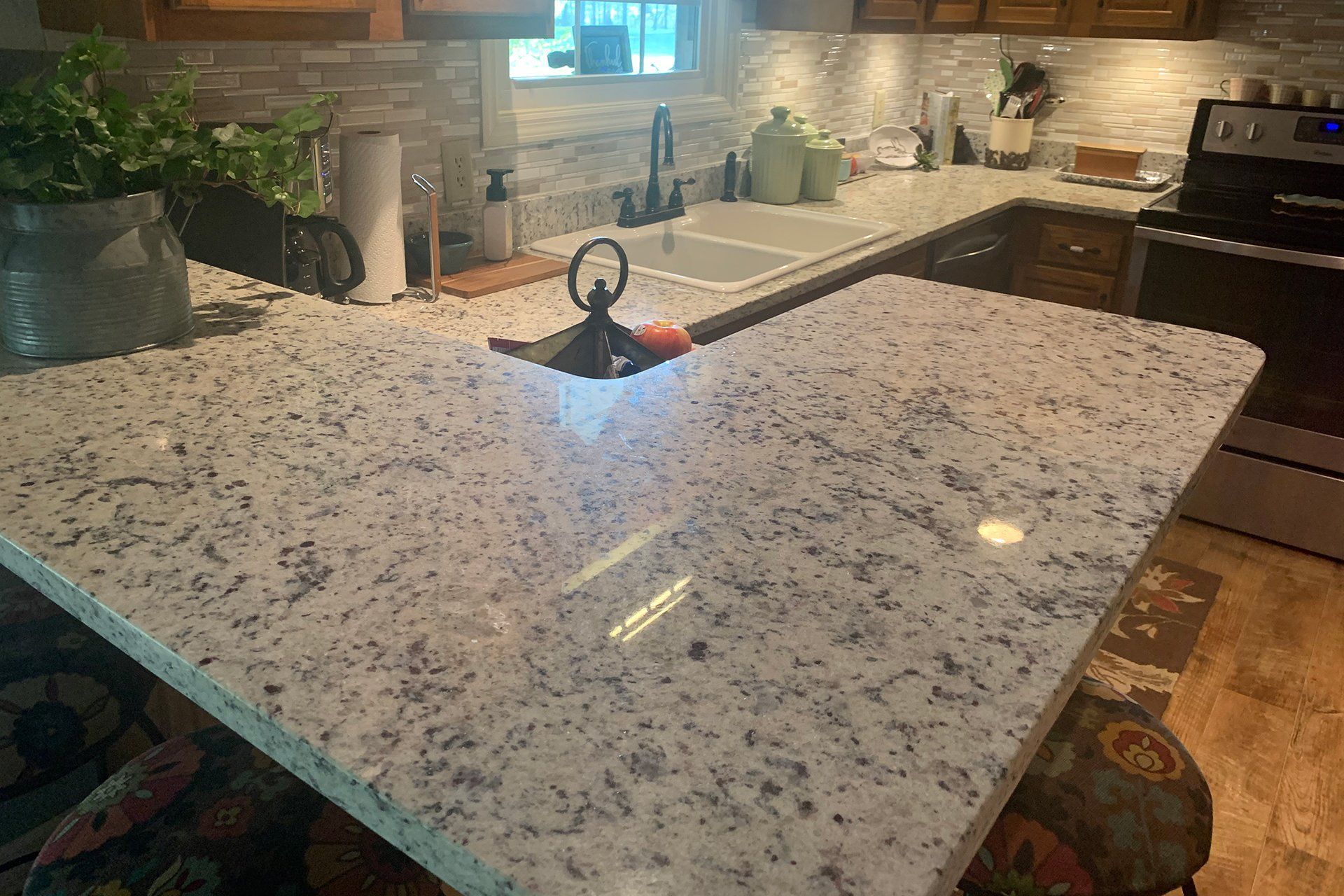 L-shaped kitchen countertop with a sink, dark faucet, and brown cabinets.  Light granite with dark flecks.