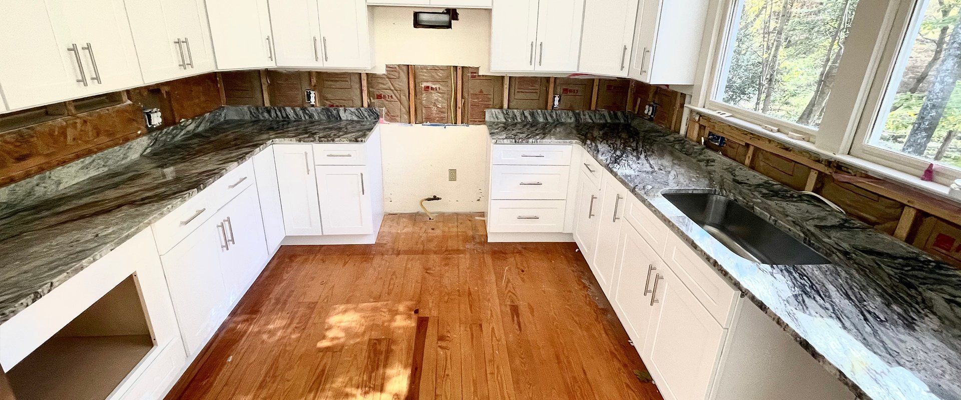 Kitchen renovation with white cabinets, granite countertops, and exposed walls. Wooden floor.