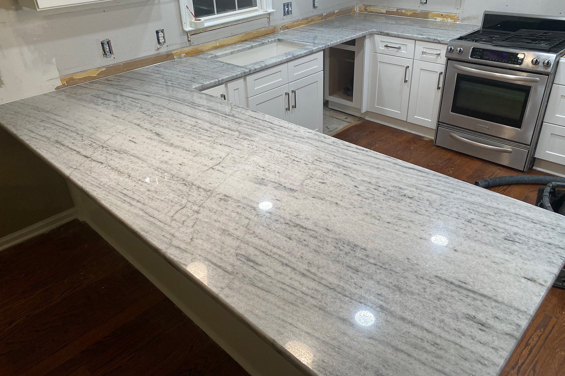 L-shaped kitchen countertop with white cabinets and a stainless steel stove, hardwood floor.