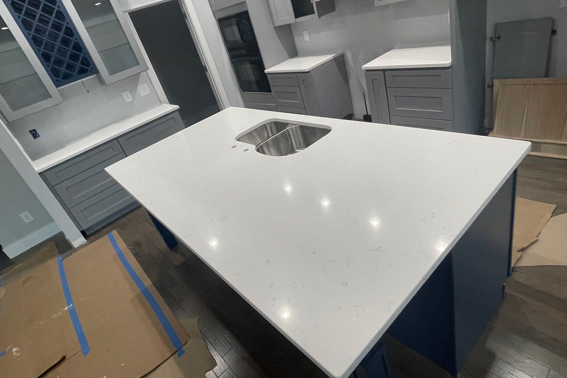 Kitchen with white countertop island and sink, blue cabinets, and gray cabinets in the background.