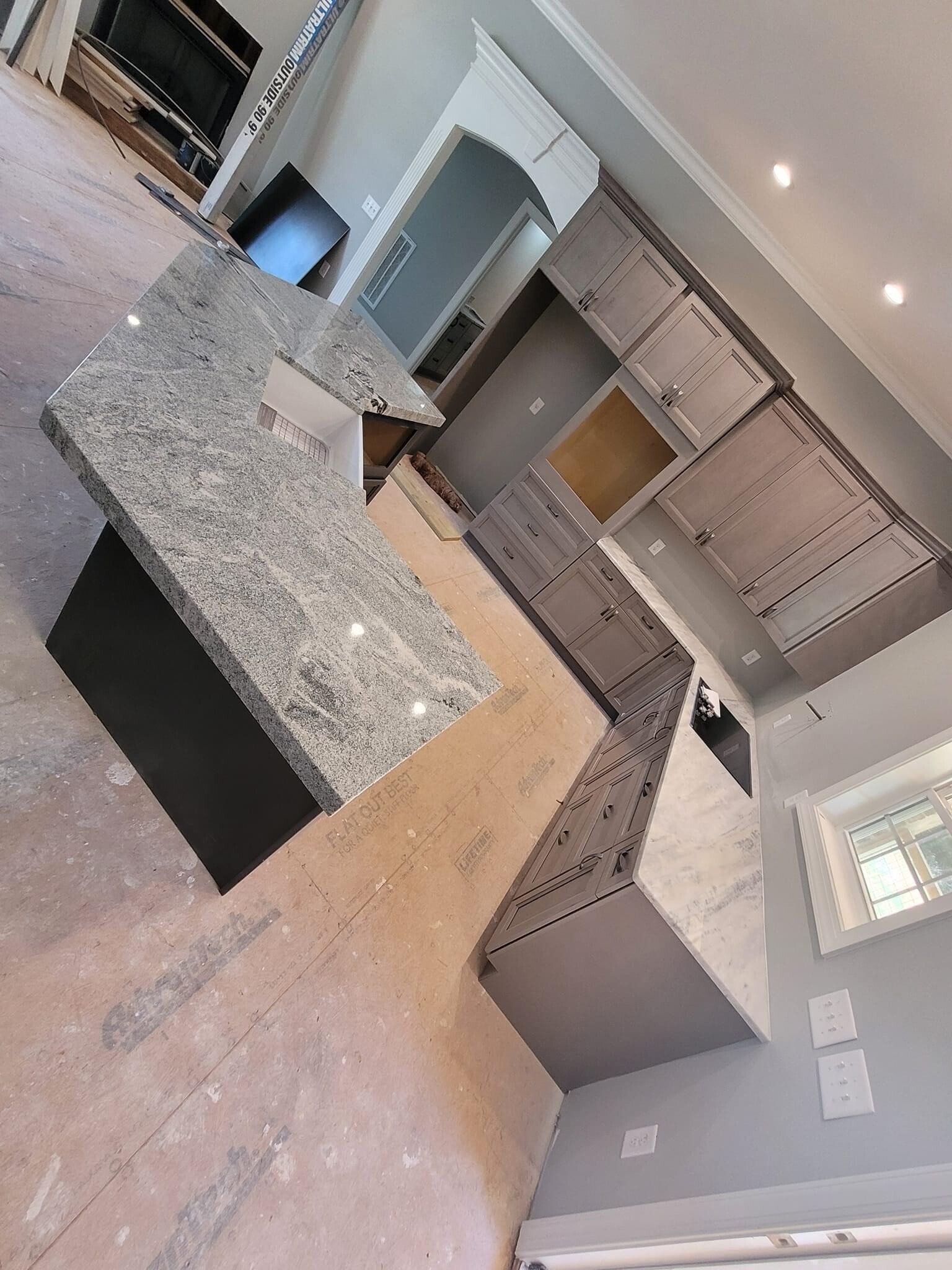 Kitchen under construction, gray cabinets and countertops, island, and exposed floor.