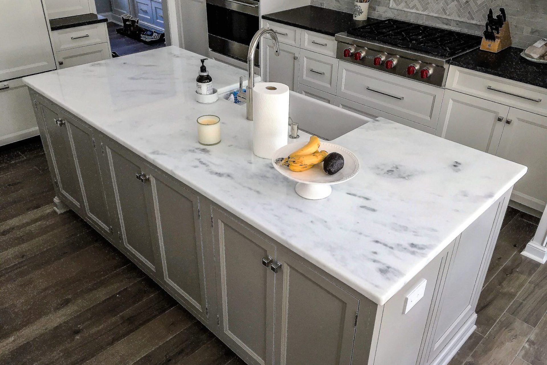 Gray kitchen island with marble countertop. White cabinets, stainless steel faucet, and wooden floor.