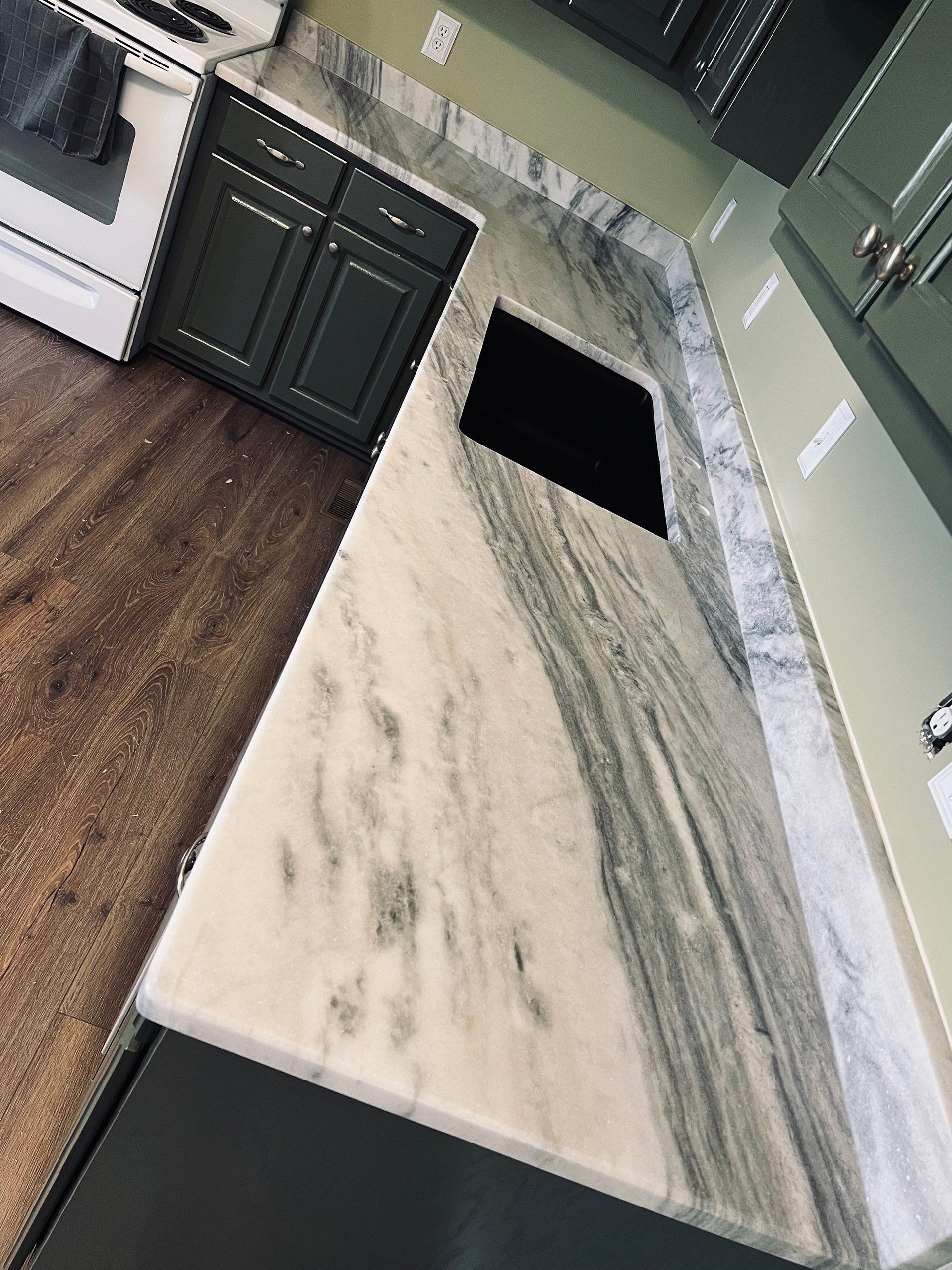 Kitchen with marble countertop, green cabinets, and wooden floor.