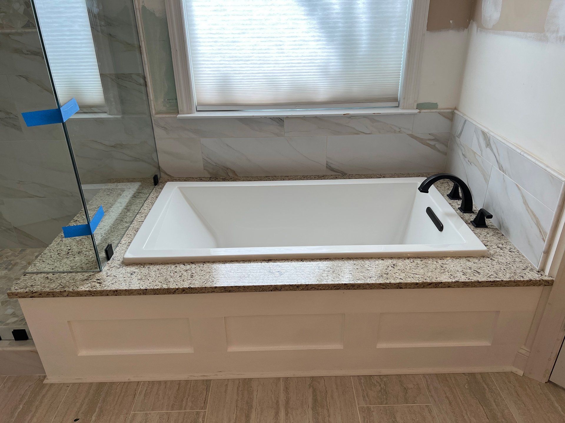 Bathroom with a white rectangular tub, granite countertop, and marble tile.