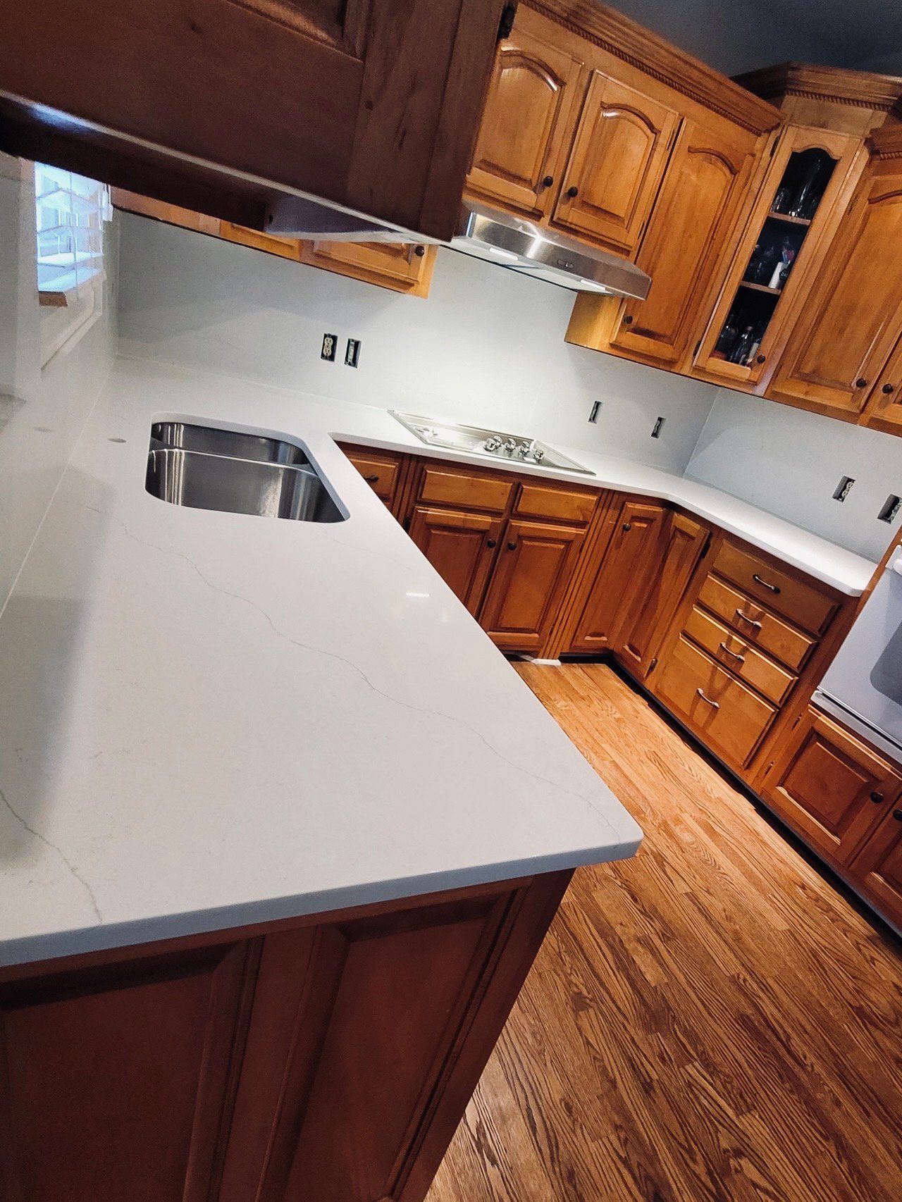 Kitchen with white countertops, wooden cabinets, stainless steel sink, and hardwood floor.