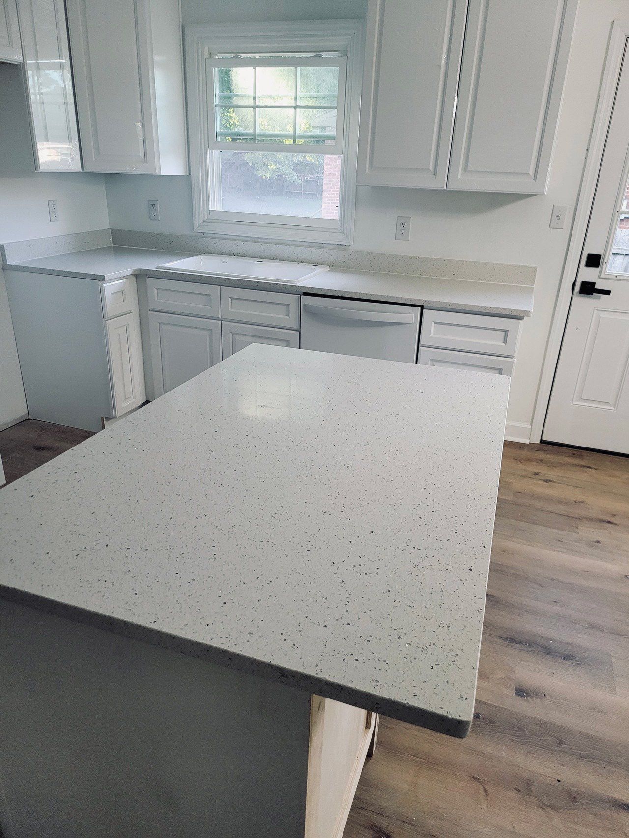 White kitchen with quartz countertops and island; window, cabinets, and dishwasher visible.