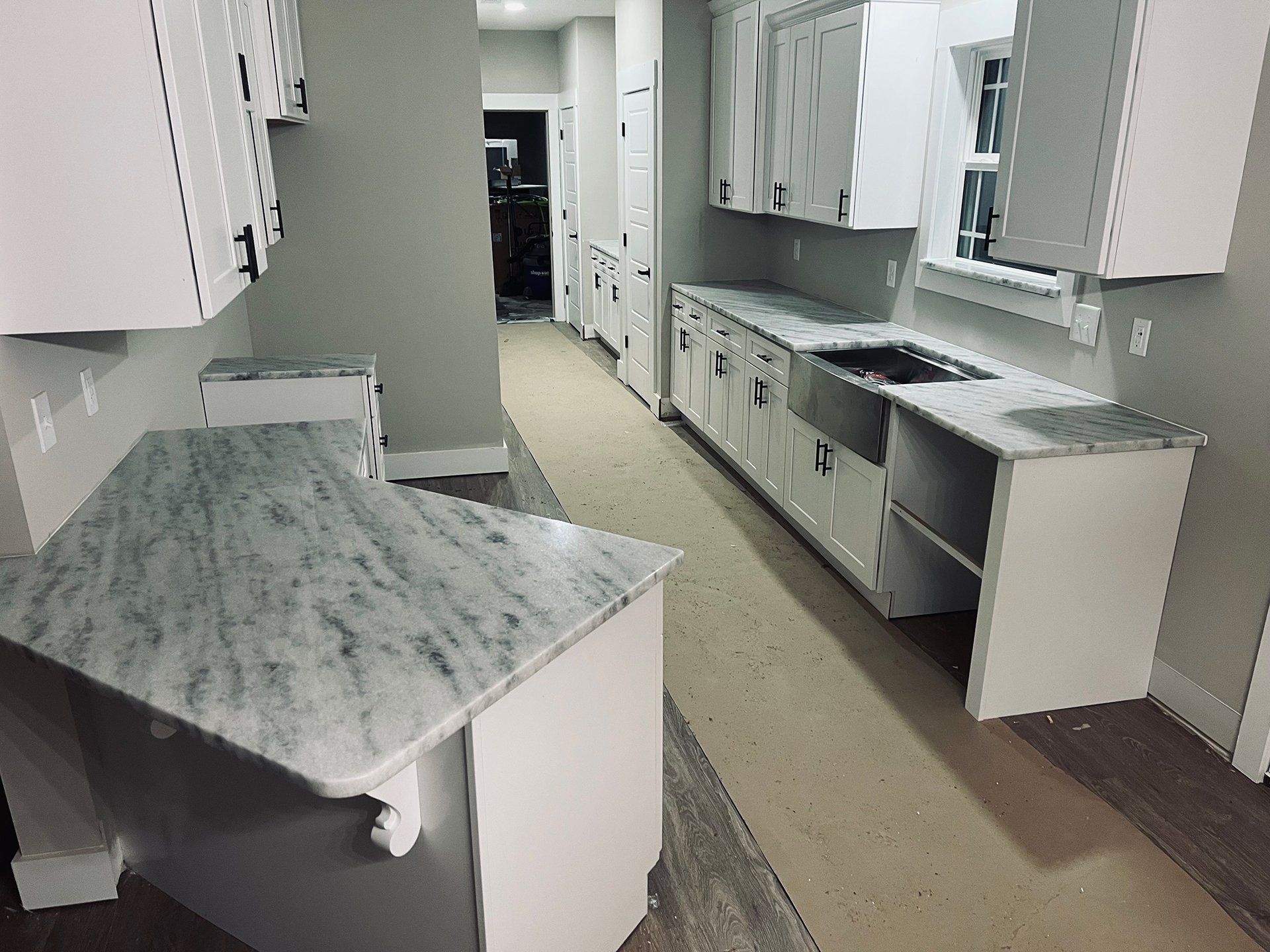 White kitchen with granite countertops, cabinets, and a stainless steel sink.