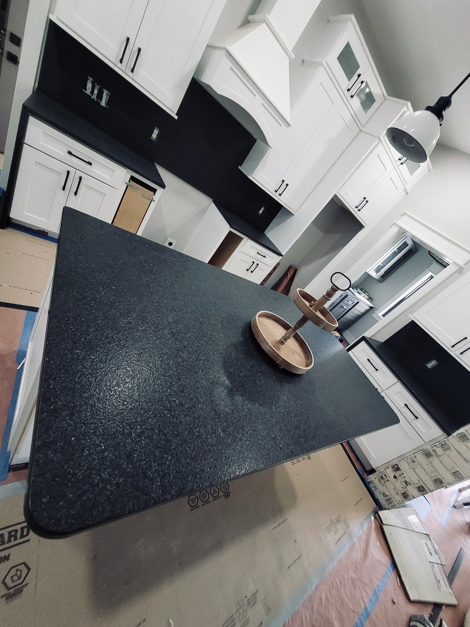 A kitchen with white cabinets, black countertops, and an island with a tiered tray, under construction.