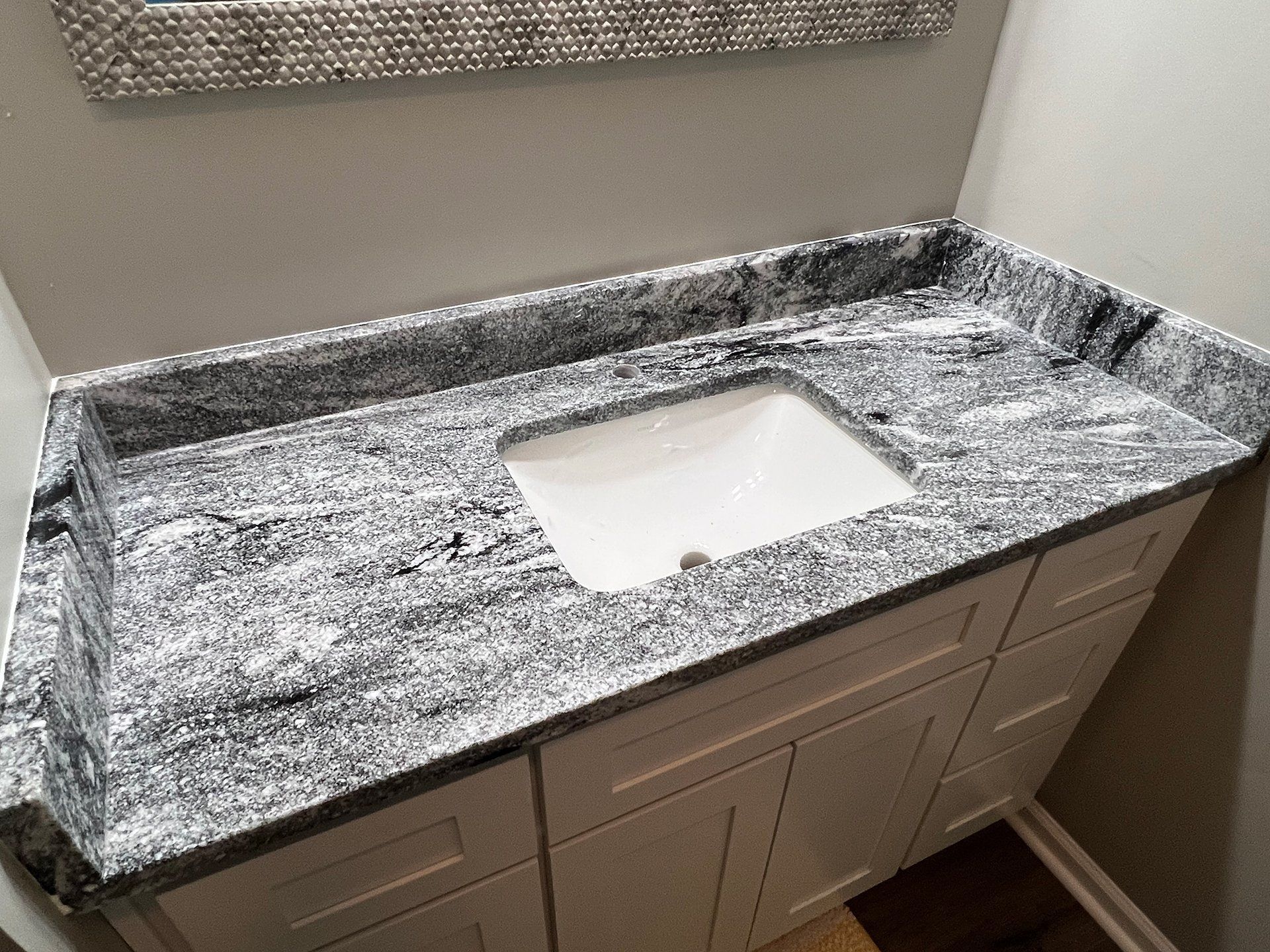 Bathroom vanity with white cabinet, granite countertop, and white sink.