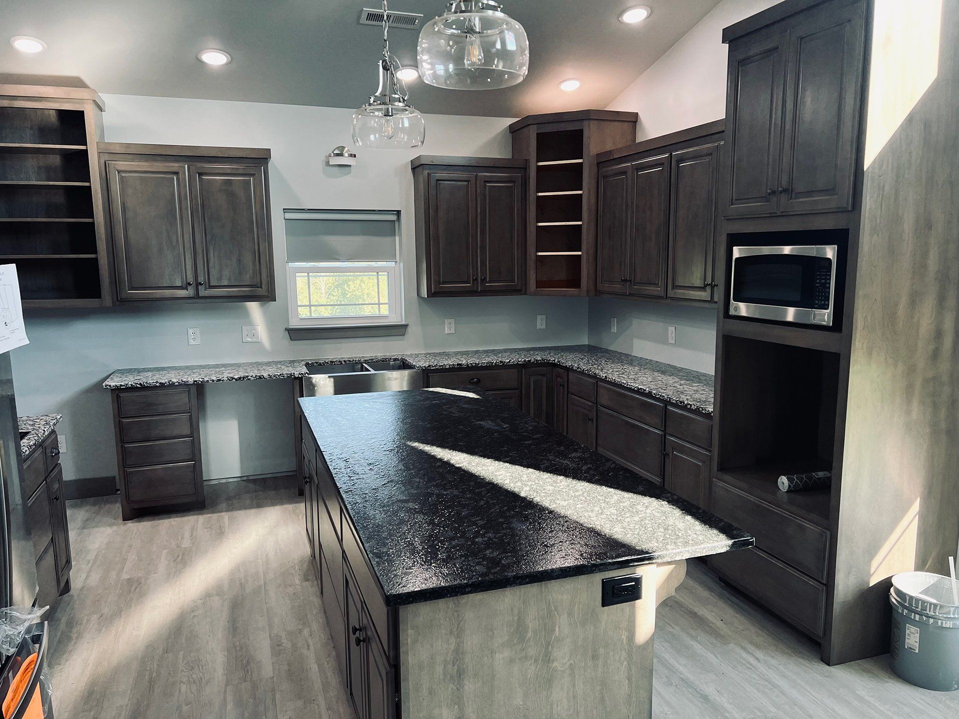 Spacious kitchen with dark cabinets, granite countertops, and a large island with a microwave and open shelves.