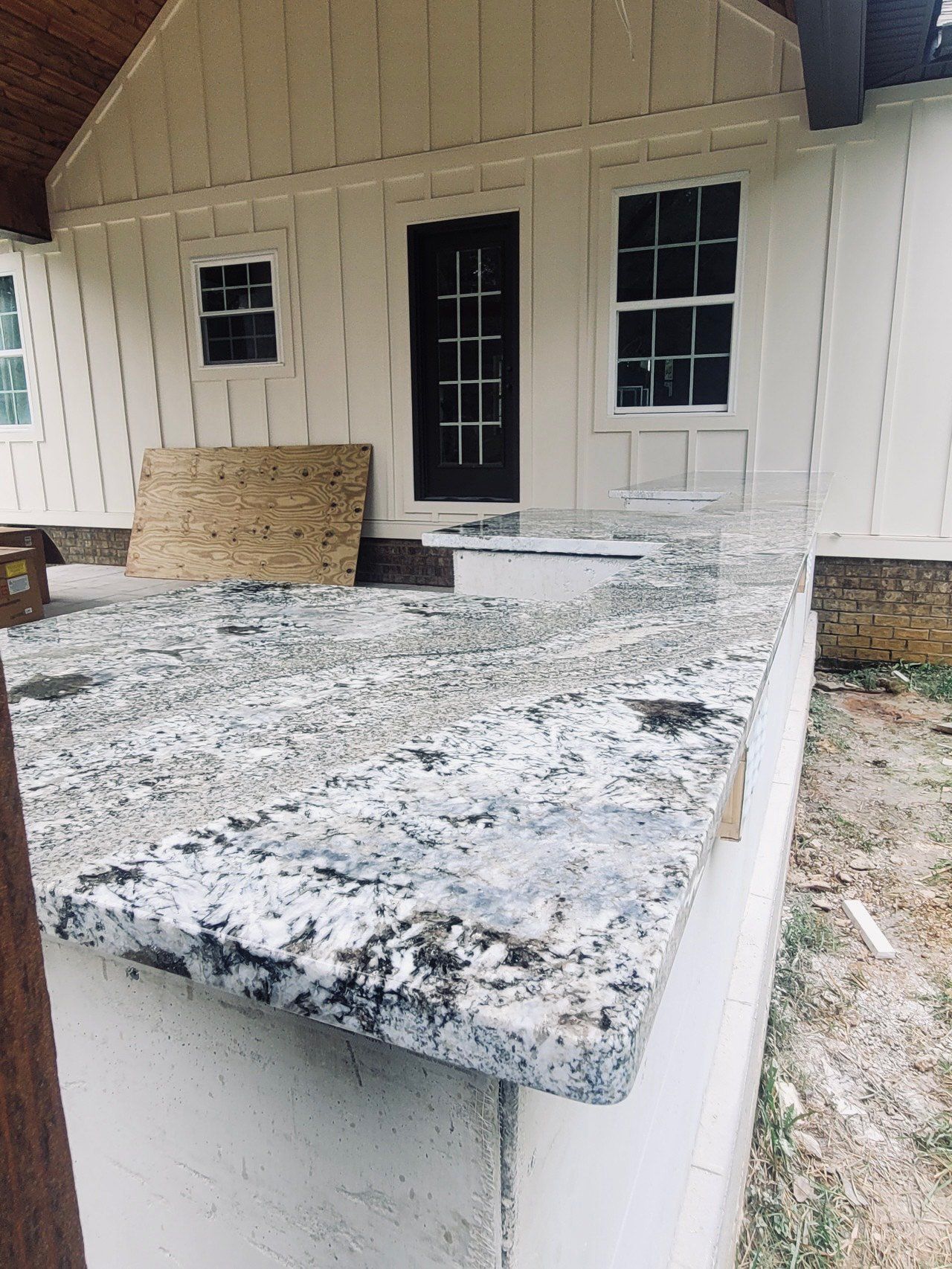 Granite countertop on a concrete porch, under a white house with a dark door.