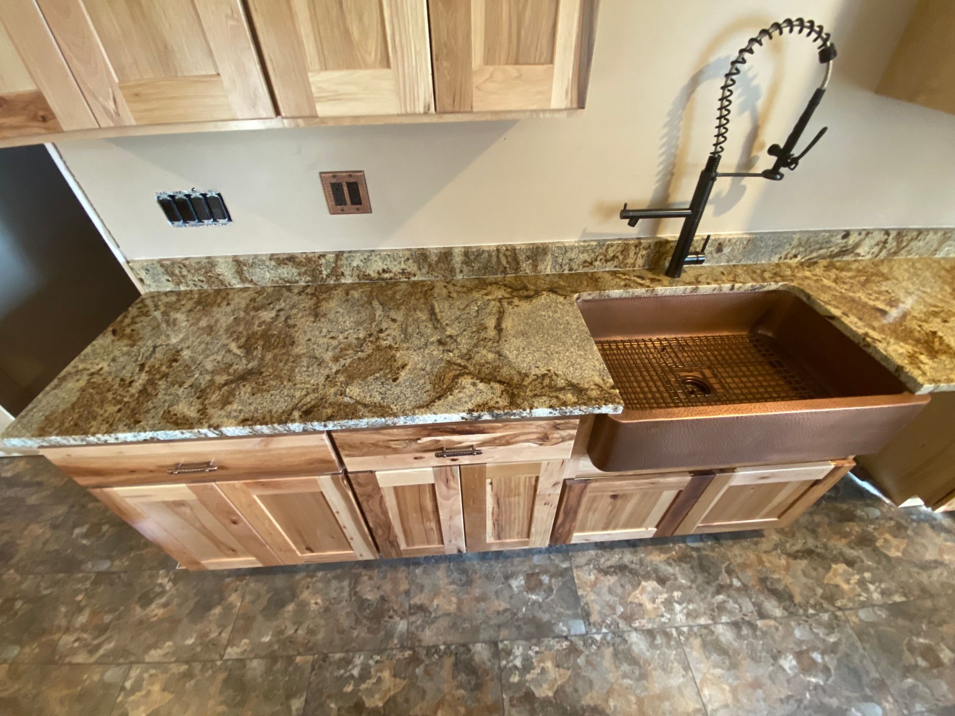 Kitchen counter with copper sink and faucet. Wooden cabinets, tan granite, and neutral wall.