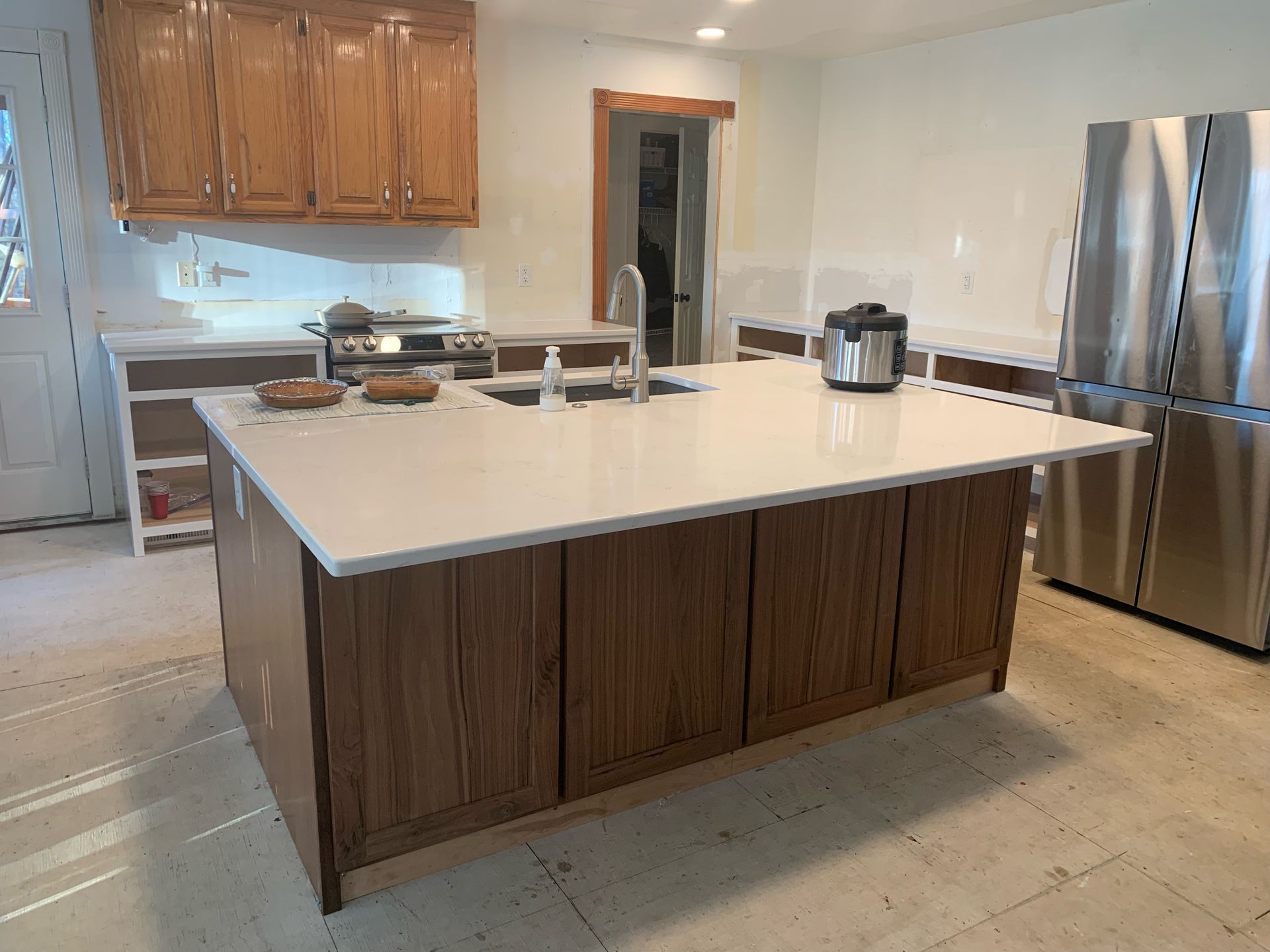 Kitchen with wood cabinets, white countertops, stainless steel fridge, and an island.