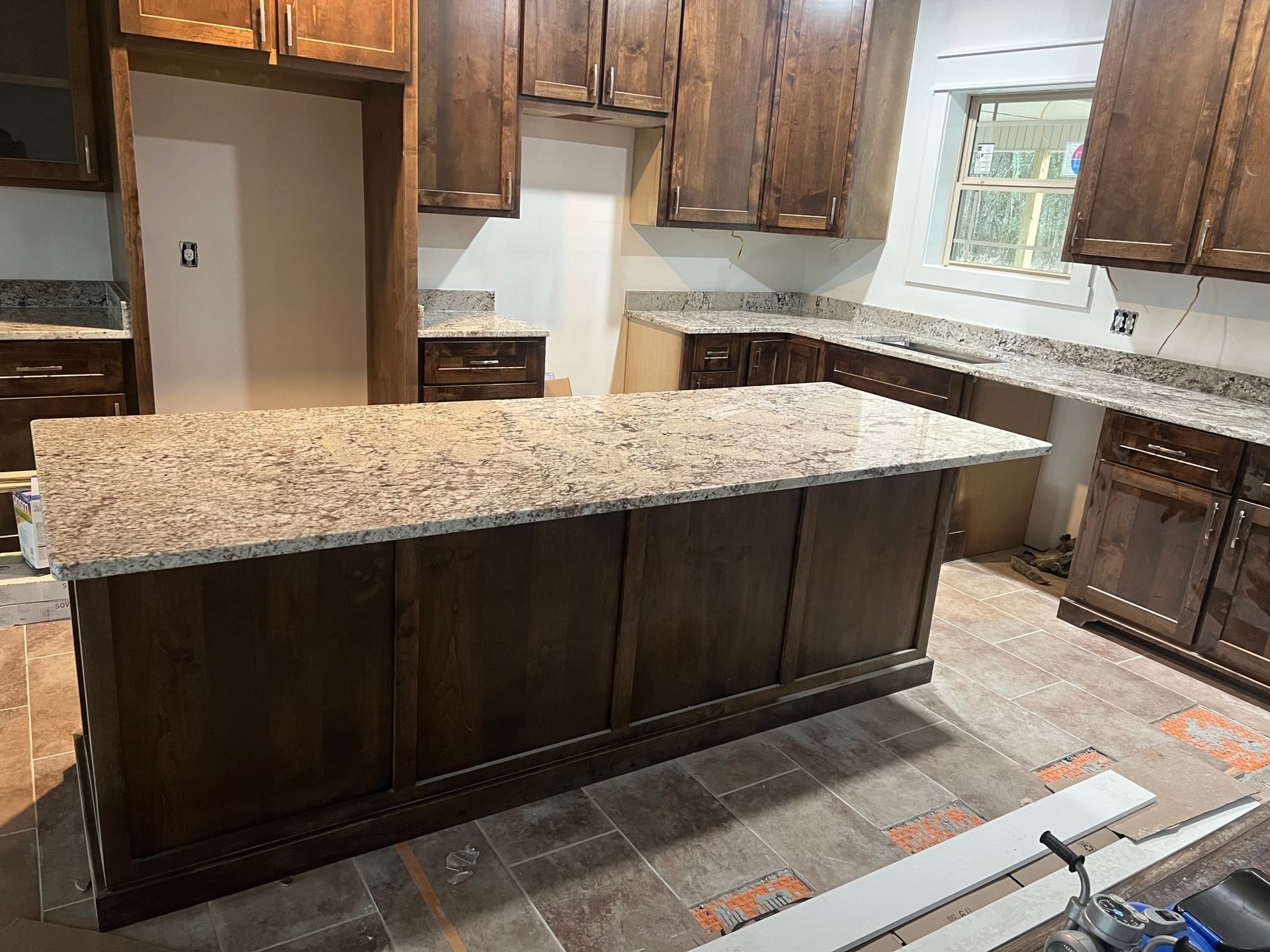 Kitchen with dark wood cabinets and island, light granite countertops, in construction phase.