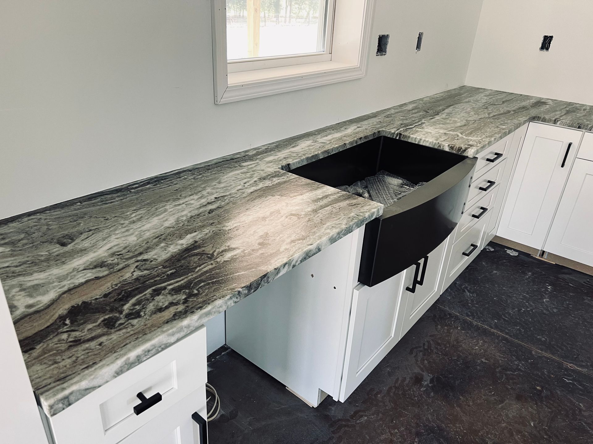 Kitchen with white cabinets, grey granite countertops, and a black farmhouse sink.