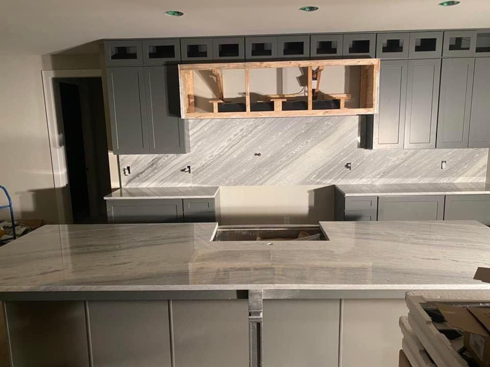 Kitchen renovation: gray cabinets, marble backsplash and island, wooden range hood frame.