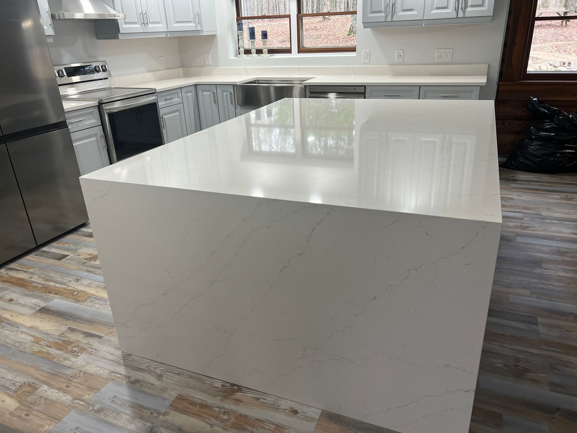 Kitchen with a large white island, gray cabinets, stainless steel appliances, and wood-look flooring.