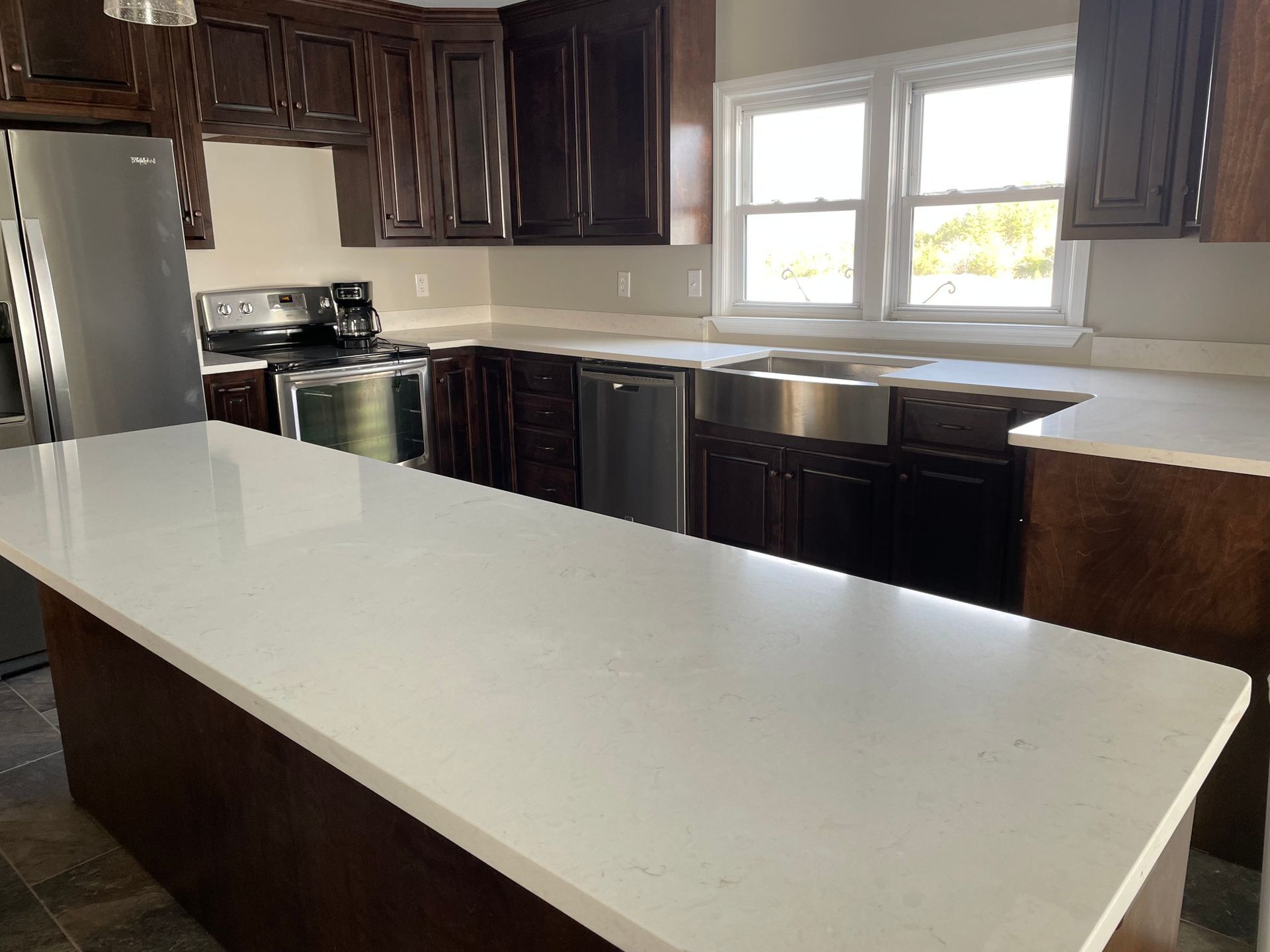Kitchen with dark brown cabinets, white countertops, stainless steel appliances, and a large island.