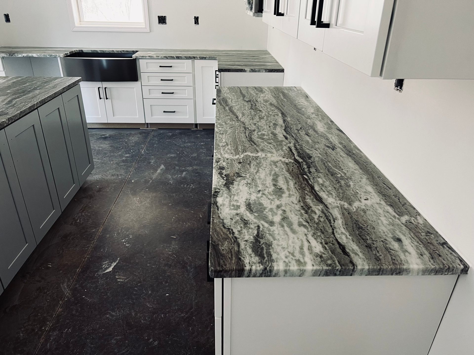 Kitchen with gray and white cabinets, dark countertops, and unfinished floor.