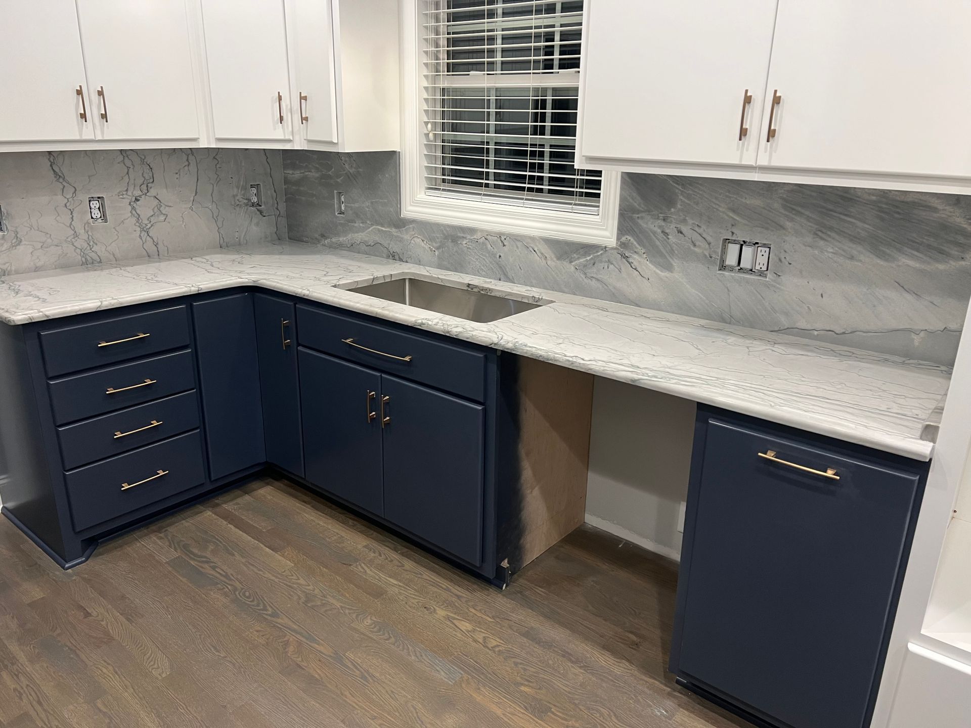 Navy blue and white kitchen with accessible countertop; gray backsplash and white cabinets.
