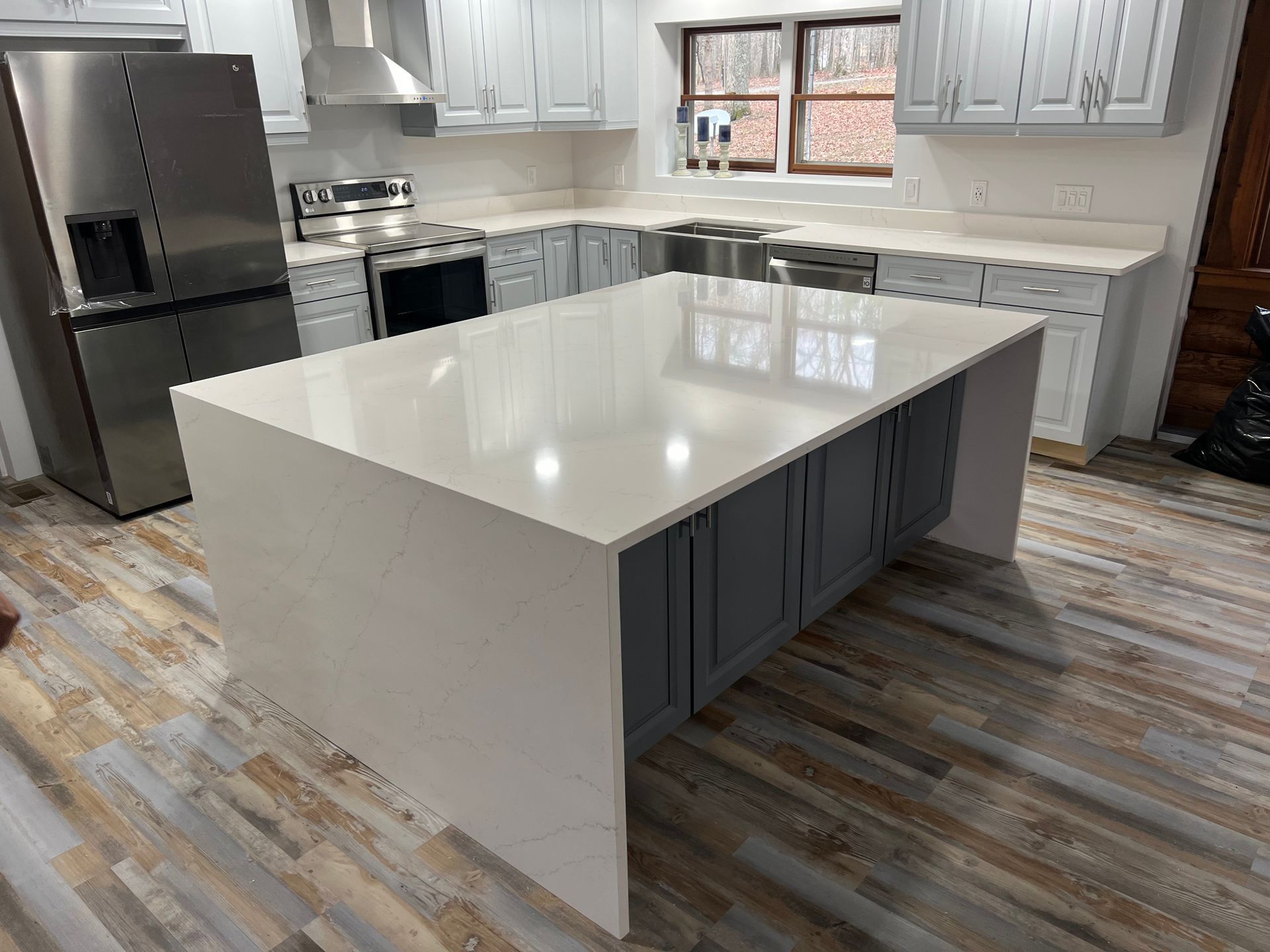 Modern kitchen with a large white island, stainless steel appliances, and light gray cabinets.