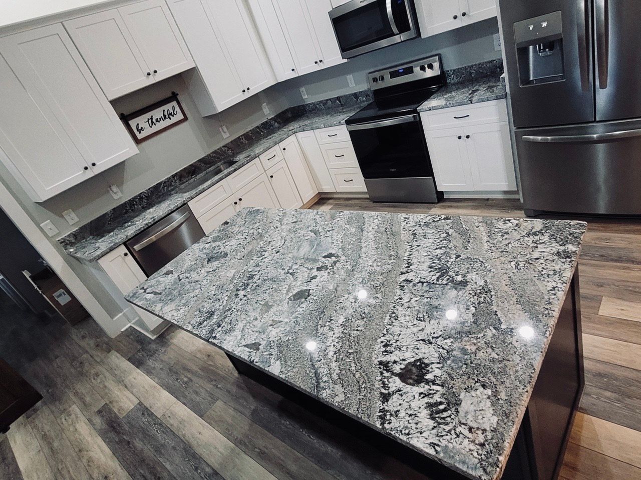 Modern kitchen with white cabinets, gray countertops, stainless steel appliances, and a patterned island countertop.