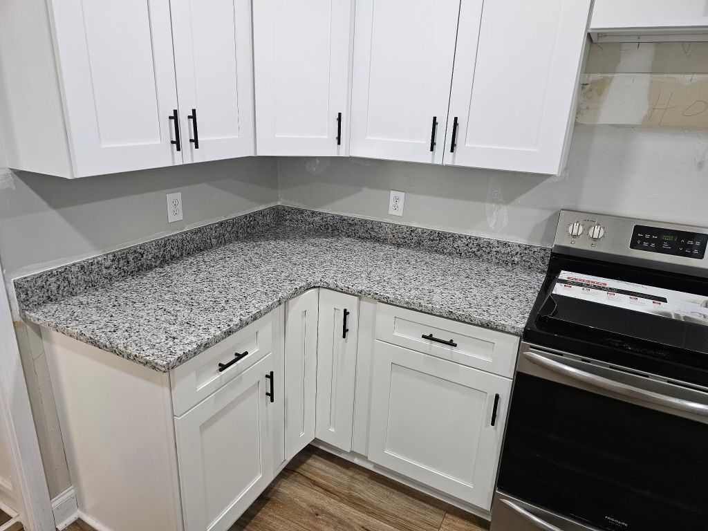 White kitchen cabinets with black hardware, gray countertop, and a stainless steel stove.