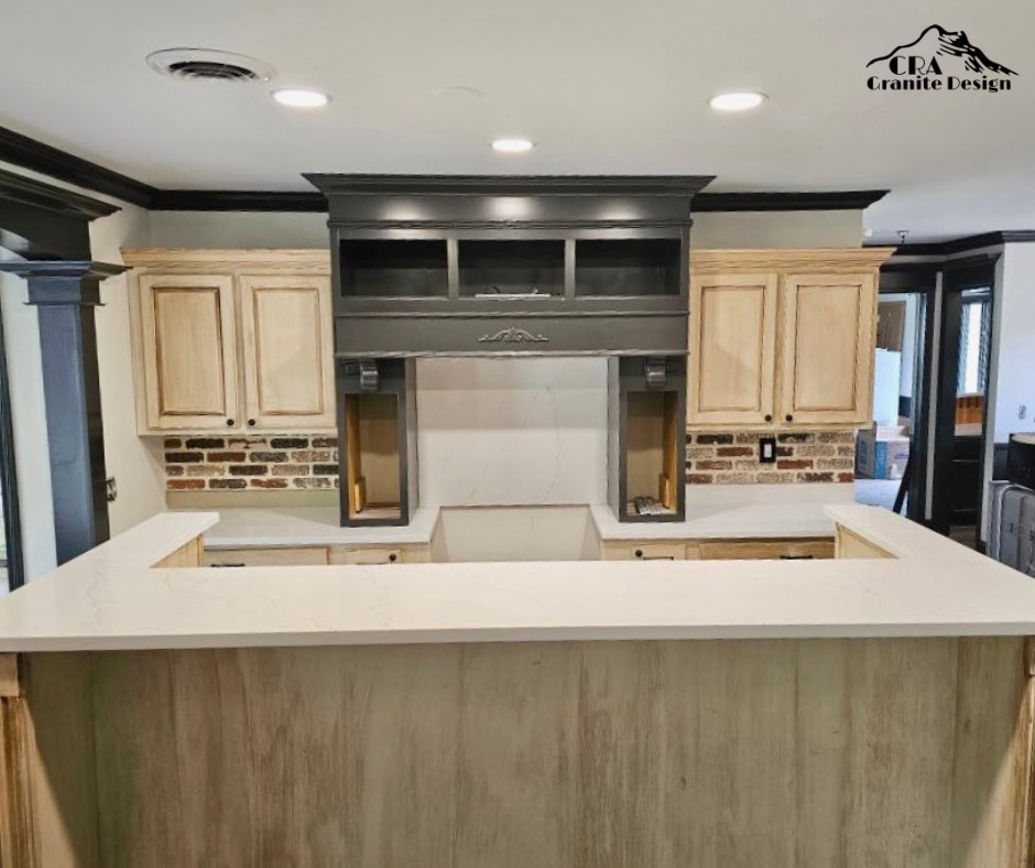 Kitchen with light countertops, cabinets, and a dark gray range hood; exposed brick backsplash.