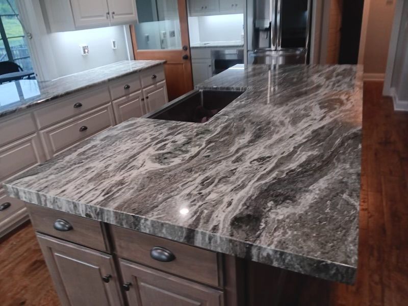 Kitchen island with gray and white marble countertop, cabinets, and a sink.