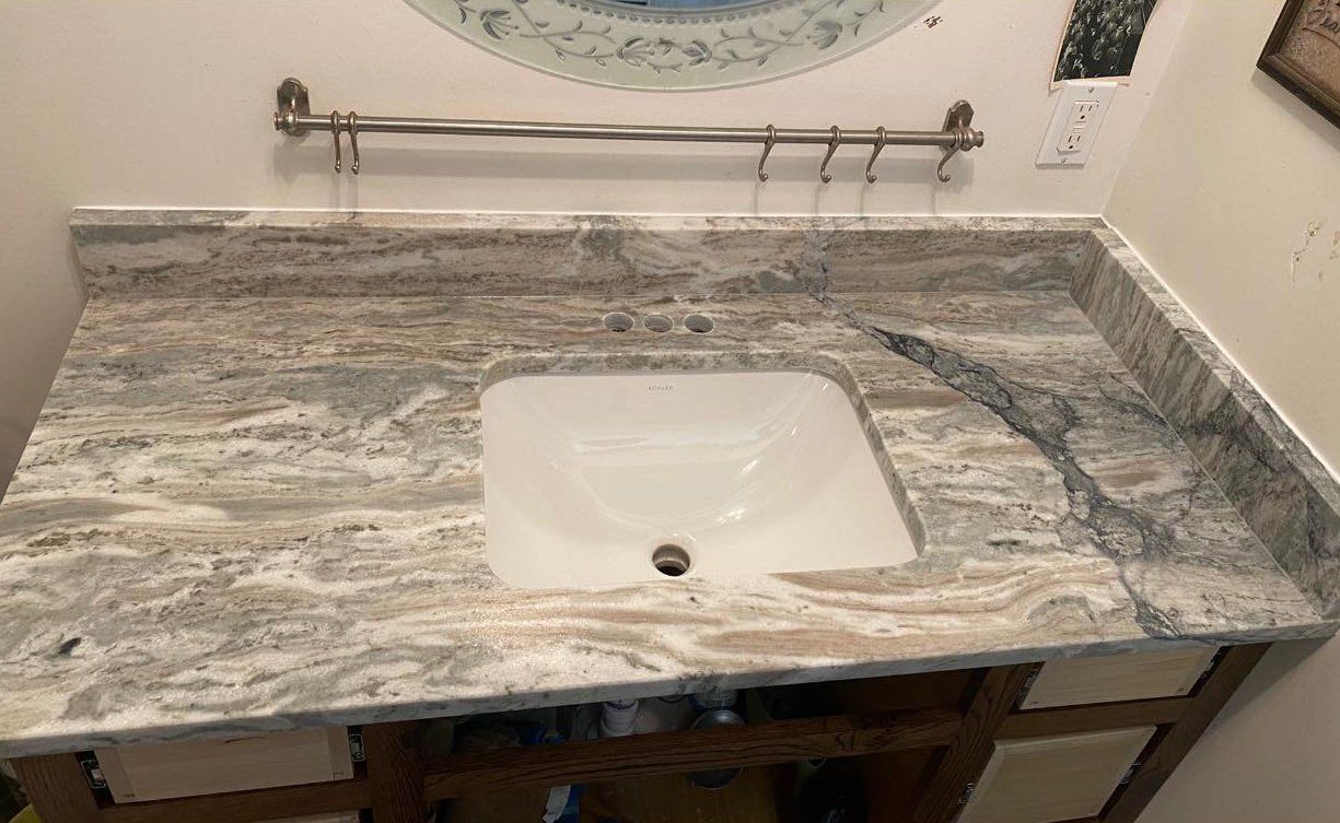 Bathroom vanity with light brown and gray granite countertop, white sink, and towel rack.