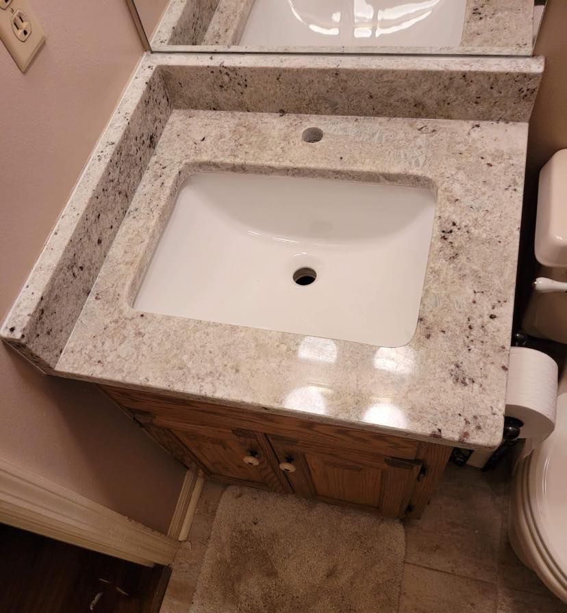 Bathroom vanity with light granite countertop, white sink, wooden cabinet, and toilet.
