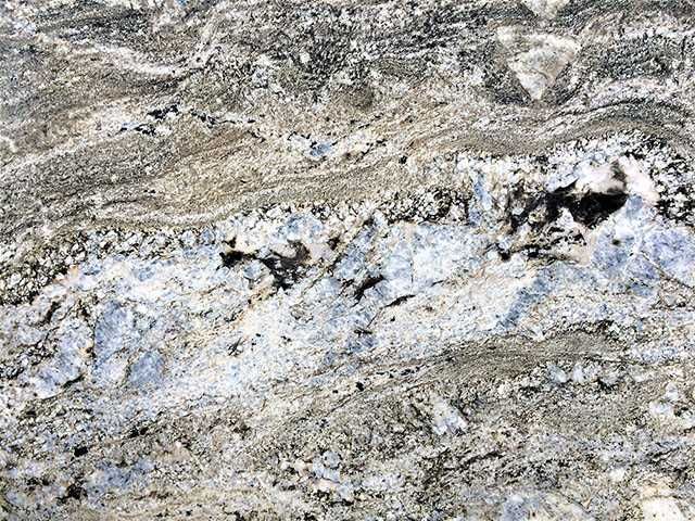 Close-up of granite with wavy, layered patterns in shades of gray, white, and hints of blue.