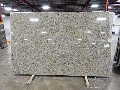 Large granite slab with gold, gray, and black flecks, indoors, resting on wooden supports.