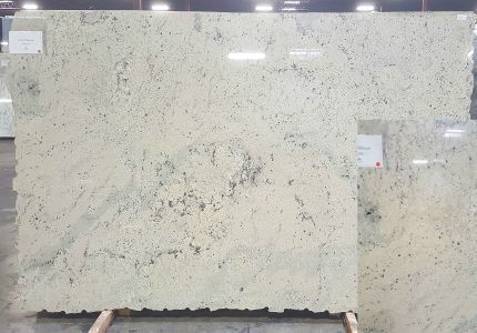 Large granite slabs with cream and black speckles, displayed on a wooden rack.
