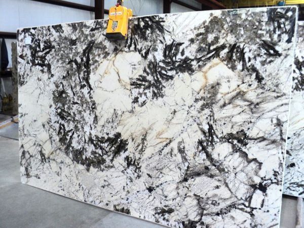 Large slab of white granite with black and gray veining, being lifted by a crane.