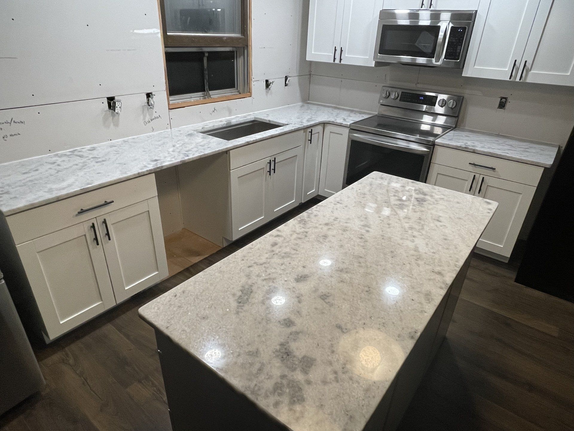 White kitchen with quartz countertops, island, and dark wood floors.