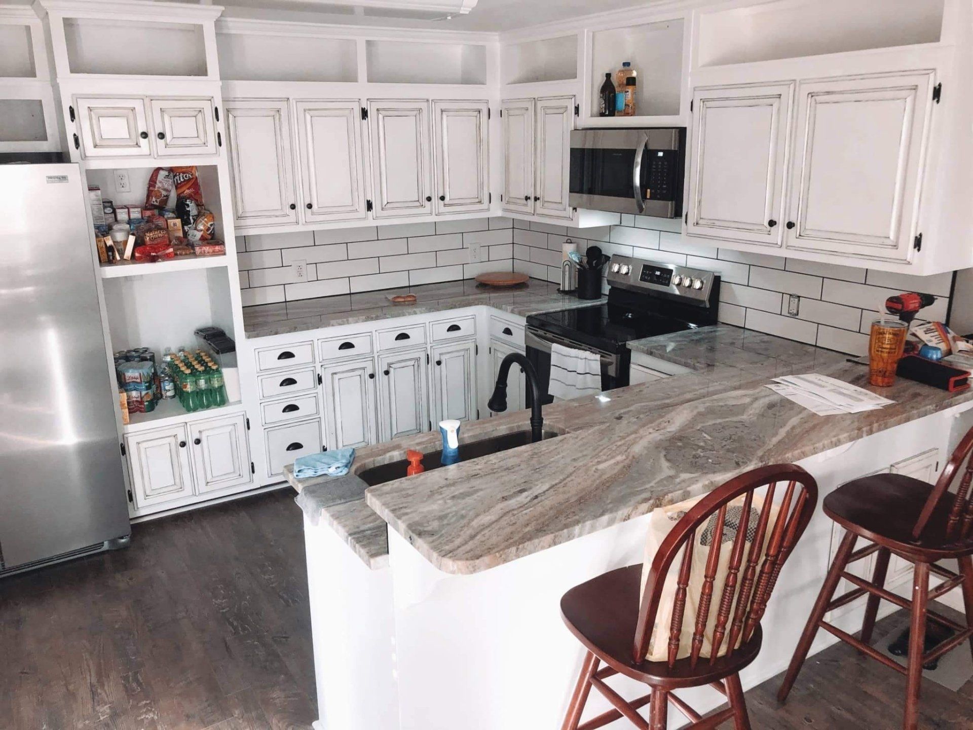 White kitchen with granite countertops, black sink, and stools. Stainless steel fridge, black stovetop.