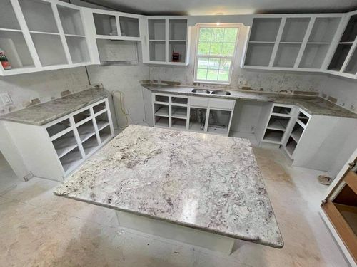 White kitchen cabinets and granite countertops in a room under renovation.
