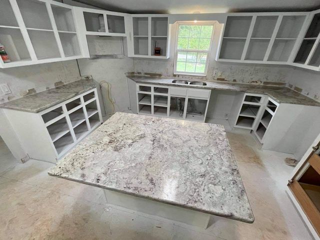 White kitchen cabinets and granite countertops in a room under renovation.