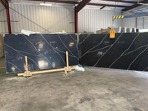 Two large, black slabs with white veining are inside a warehouse. They lean against a wall.