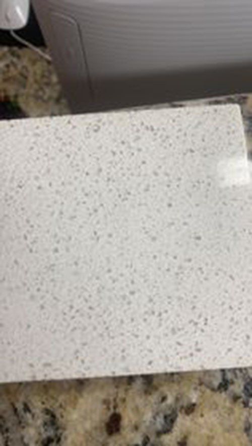 White quartz countertop with speckled gray patterns, set on a patterned countertop.