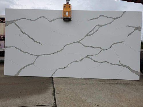 Large white quartz slab with grey veining being lifted by a crane.