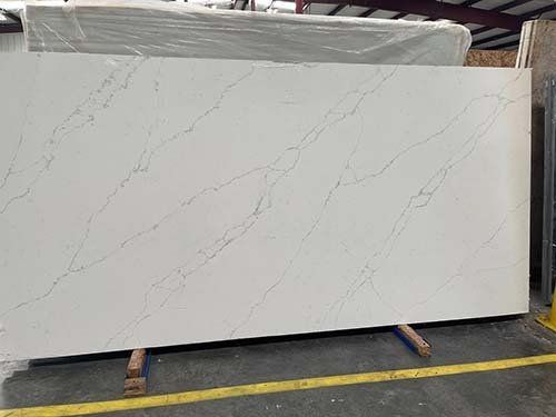 White quartz countertop slab with gray veining, leaning against a wooden stand in a warehouse.