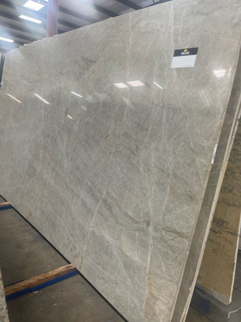 Large beige stone slab, veined with lighter and darker markings, leaning against a rack in a warehouse.