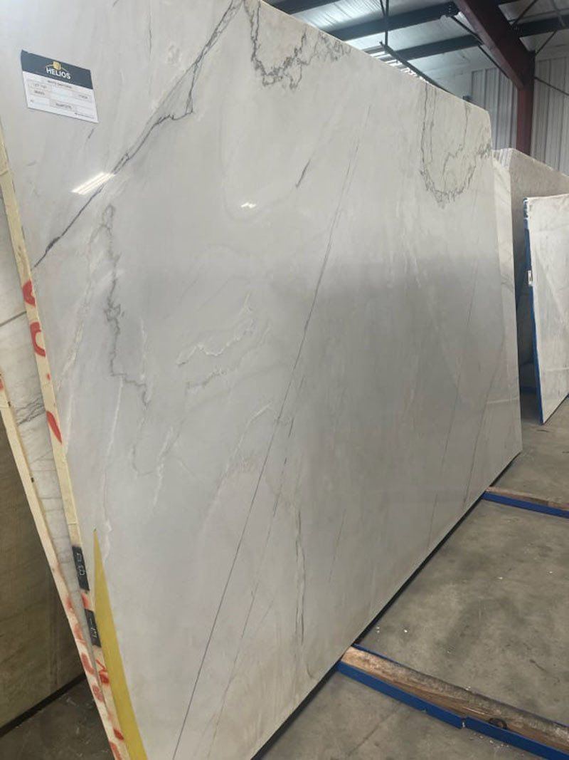 Large, light-colored marble slab with gray veining, leaning against other slabs in a warehouse setting.