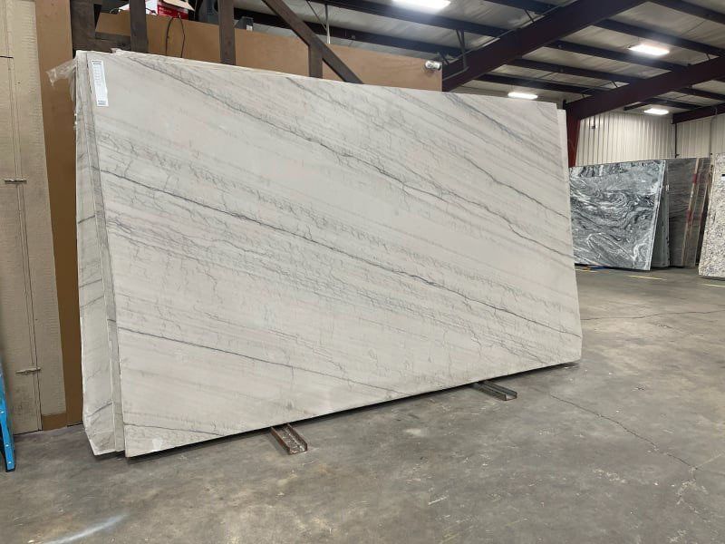 Large light stone slab with diagonal gray veining, in a warehouse setting.