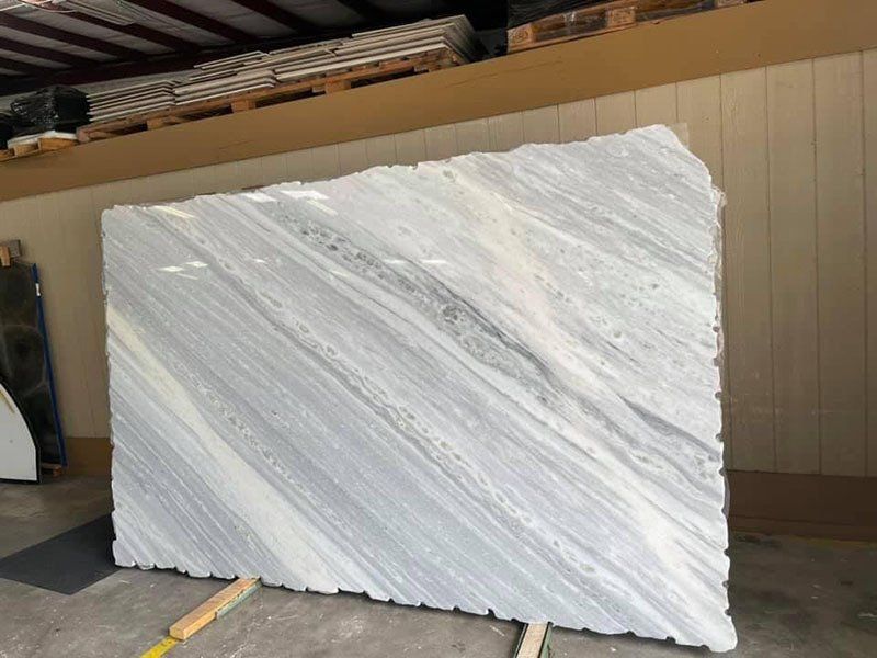 Large slab of white and gray marble with diagonal veining, displayed in a warehouse.