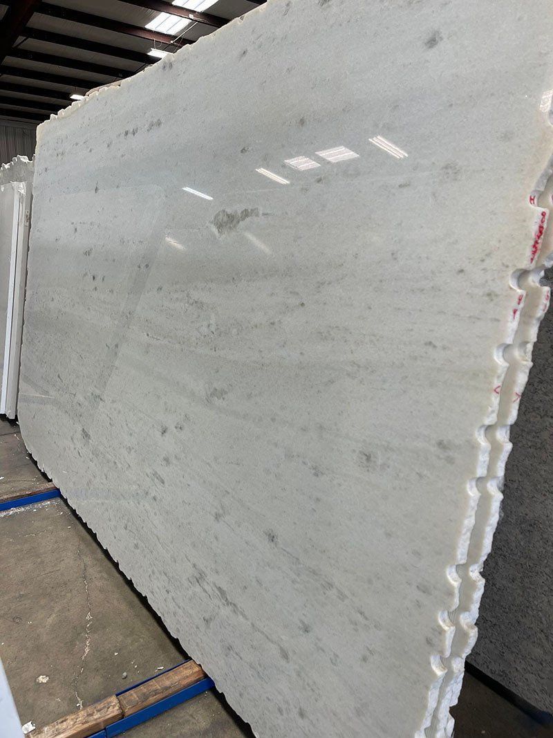 Large, light-colored marble slab with gray veining and speckled patterns, stacked on top of other slabs.