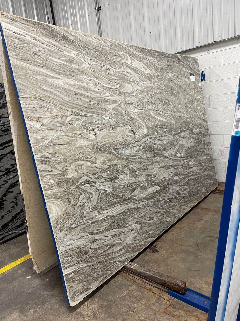 Large slab of light brown granite with swirling patterns, leaning on a rack.