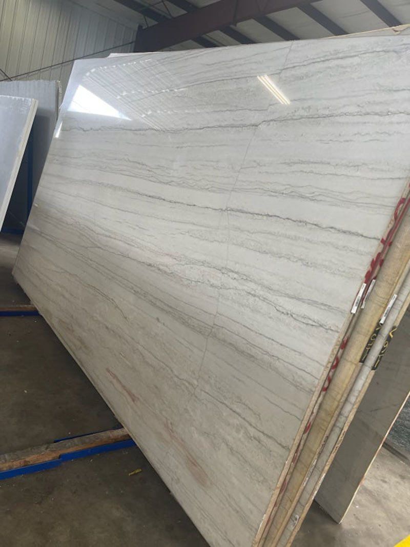 Large slab of white marble with gray veining, leaning against other slabs in a warehouse.